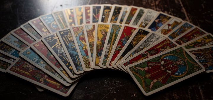 Jeu de 32 cartes étalé sur une table sombre, mettant en valeur les quatre couleurs de cartomancie avec un éclairage cinématographique et un rendu très détaillé.